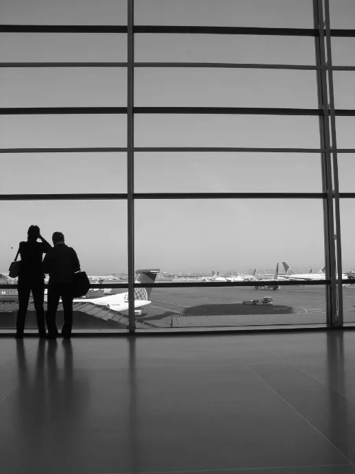 Travelers watching planes at an airport window while deciding how to choose the right travel agent.